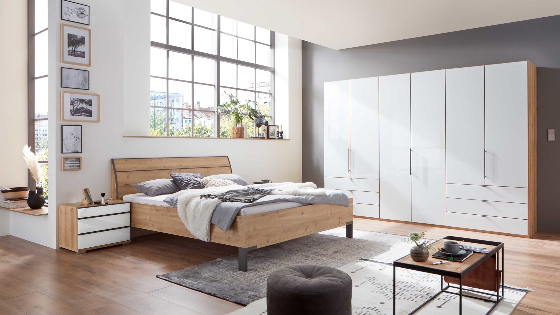 Helles Schlafzimmer im industriellen Stil mit Holz-Doppelbett, weissem Kleiderschrank und hoher Fensterfront